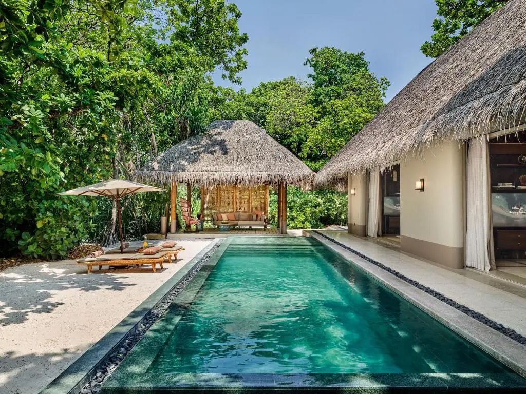 Langgestreckter Privatpool mit Sonnenliegen und reetgedecktem Pavillon im Grünen.