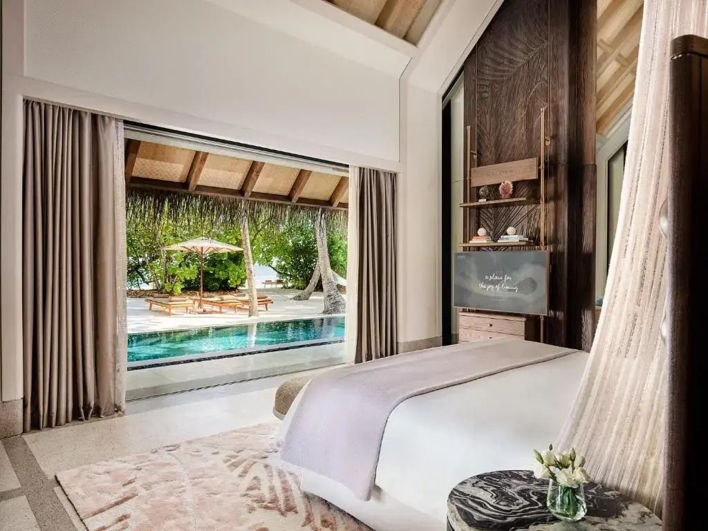 Blick aus dem Schlafzimmer auf eine Terrasse mit privatem Pool, Liegen und Strand.