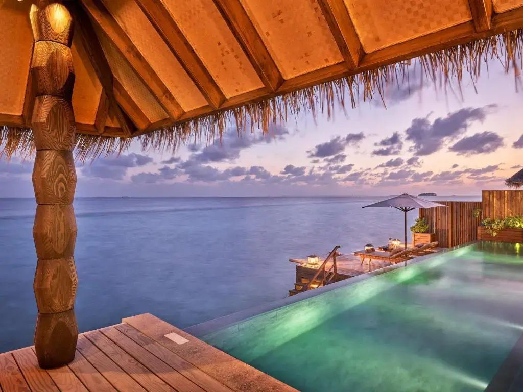 Infinitypool auf einer Stelzenvilla bei Sonnenuntergang mit Blick auf den Ozean.