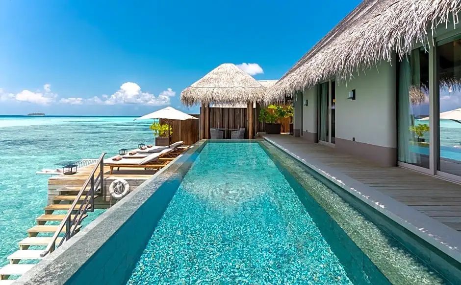 Langgestreckter privater Pool auf der Holzterrasse einer Villa mit Strandliegen und Sonnenschirm.