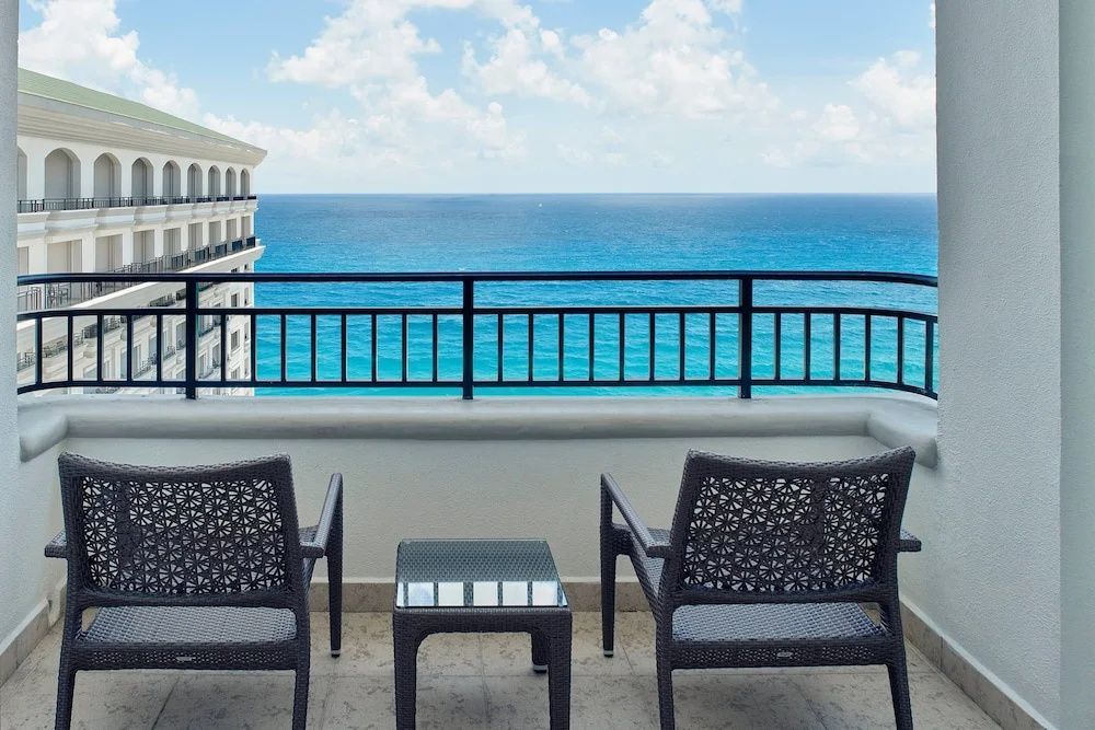 Balkon mit zwei Stühlen und einem kleinen Tisch sowie Blick auf das blaue Meer unter wolkenlosem Himmel.