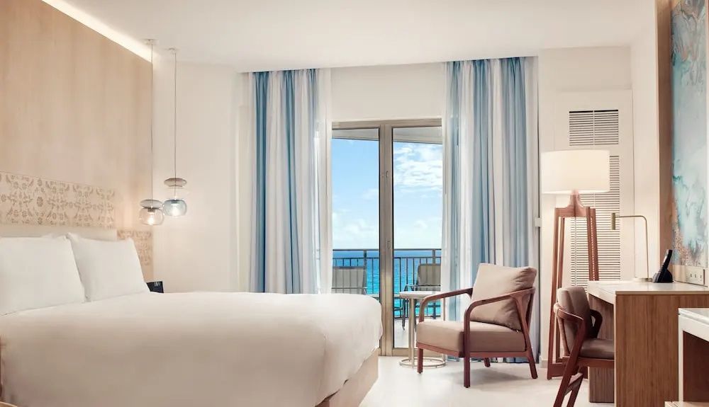 Hotelzimmer mit Sessel und Balkontür mit direktem Blick auf das blaue Meer.