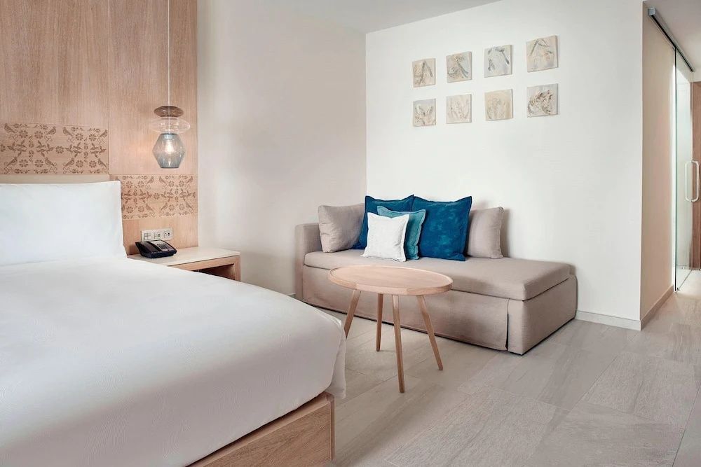 Sitzbereich im Hotelzimmer mit einem Schlafsofa, blauen Kissen und einem kleinen Holztisch.