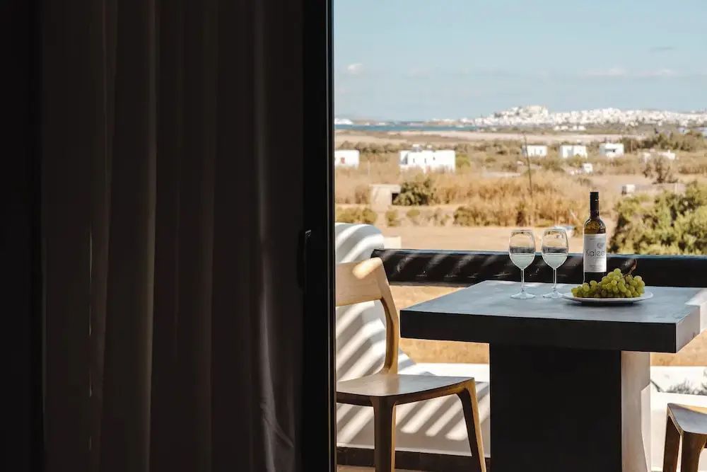 Blick von einer überdachten Terrasse mit Tisch und Stühlen auf die Küste und das Meer.