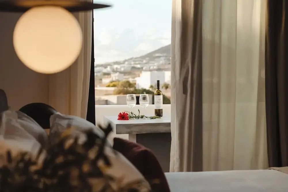 Blick durch das Fenster auf einen Tisch mit Weinflasche, Gläsern und die umliegende Landschaft.