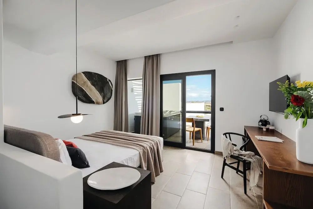 Schlafzimmer mit Doppelbett, hellem Fliesenboden und Glasschiebetür zur Terrasse.