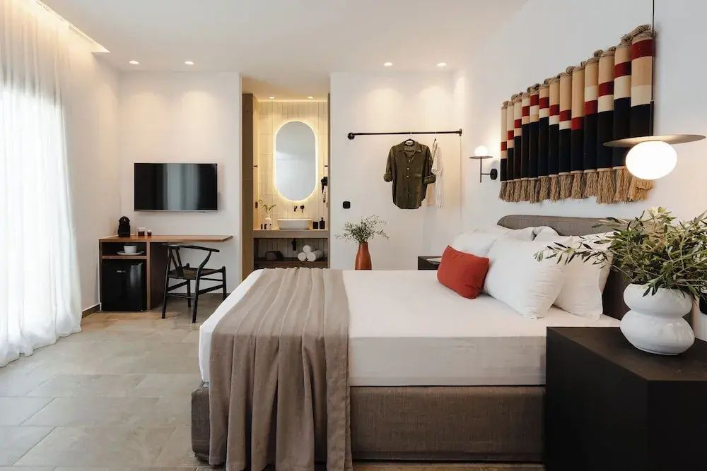 Doppelbett mit weißer Bettwäsche, Schreibtisch mit TV und Blick in das offene Badezimmer im Hintergrund.
