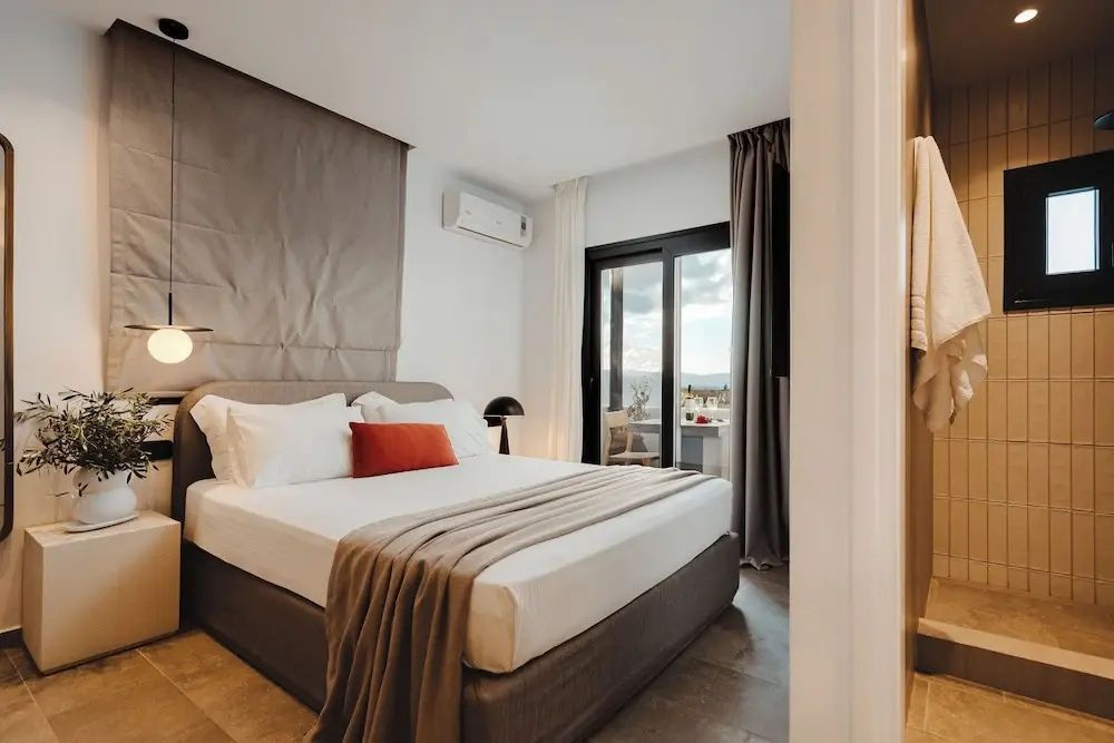 Schlafzimmer mit Doppelbett, weißer Bettwäsche und Zugang zum Balkon durch Schiebetüren.