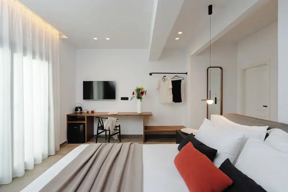 Hell eingerichtetes Zimmer mit Holzschreibtisch, Wandfernseher und Doppelbett.