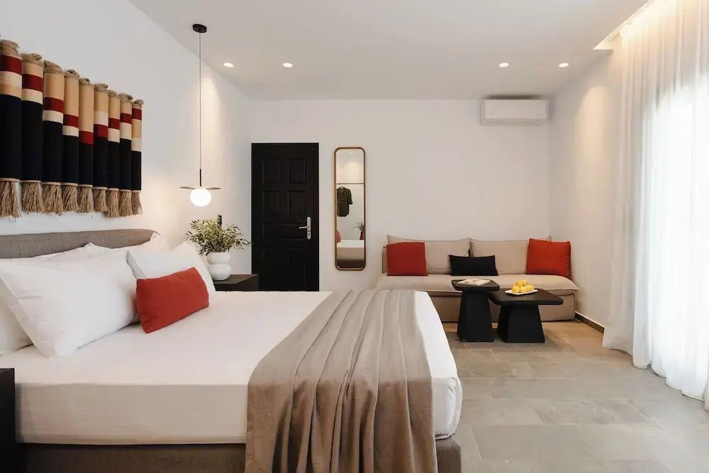 Schlafzimmer mit beigefarbenem Sofa, roten Kissen, schwarzen Beistelltischen und Wandspiegel.