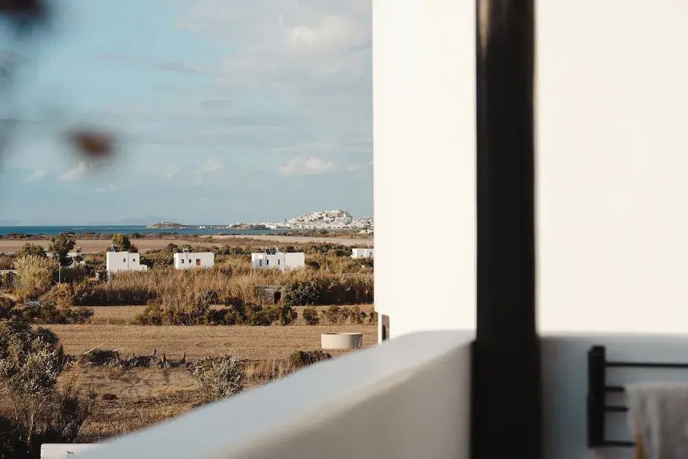 Ausblick von der Terrasse über Felder und weiße Häuser hin zum Meer unter blauem Himmel.