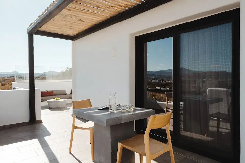 Überdachte Terrasse mit einem Tisch, zwei Stühlen und Blick auf die Umgebung.
