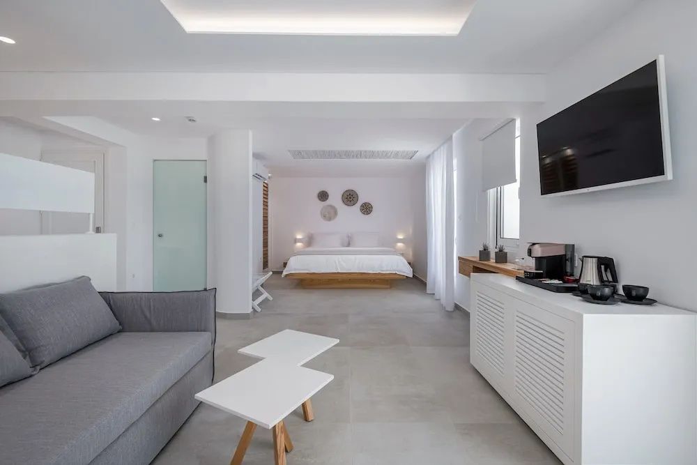 Helles, modern eingerichtetes Hotelzimmer mit Doppelbett, grauem Sofa und Beistelltischen.