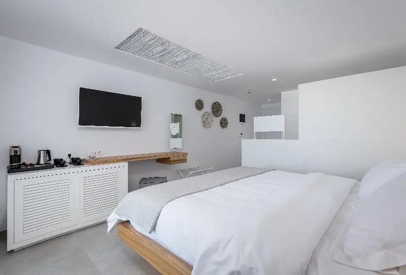 Weiss eingerichtetes Hotelzimmer mit Doppelbett, Flachbildfernseher an der Wand und Holzdekor.