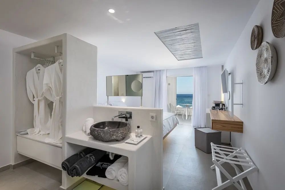 Offenes Hotelzimmer mit integriertem Waschtisch, Bett und Blick auf das Meer