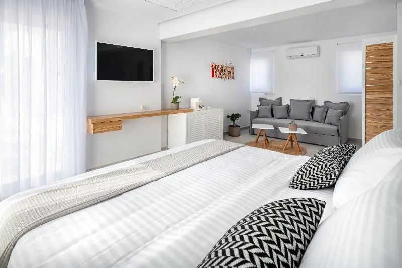 Modernes Hotelzimmer mit grossem Doppelbett im Vordergrund und Sitzecke mit grauem Sofa im Hintergrund.