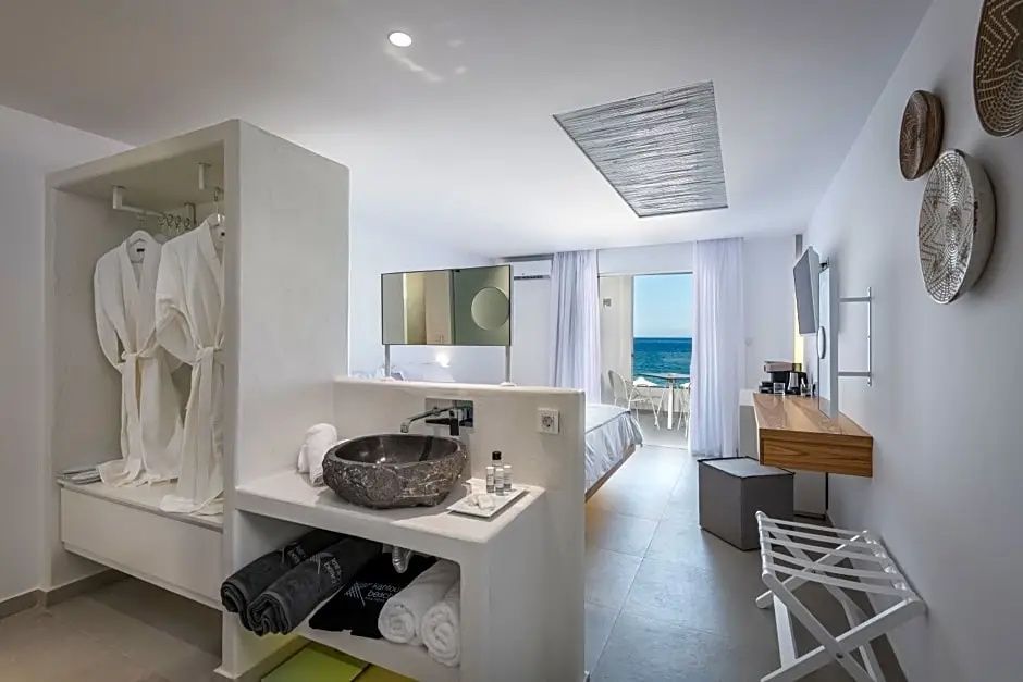 Offener Schlafbereich und Waschbereich im Zimmer mit Steinwaschbecken und Meeresblick.