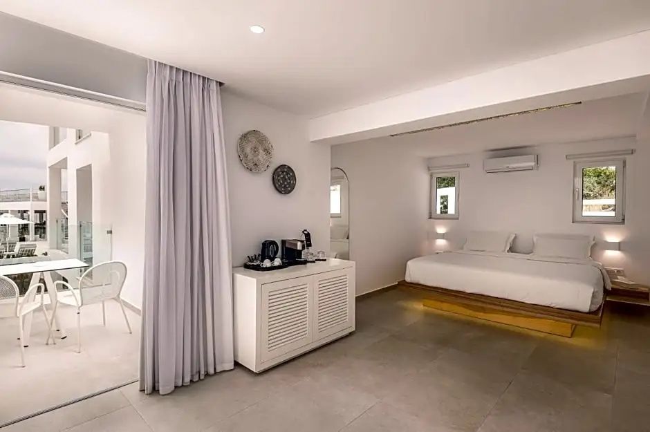 Weiß eingerichtetes Hotelzimmer mit Doppelbett auf Podest und Kommode.