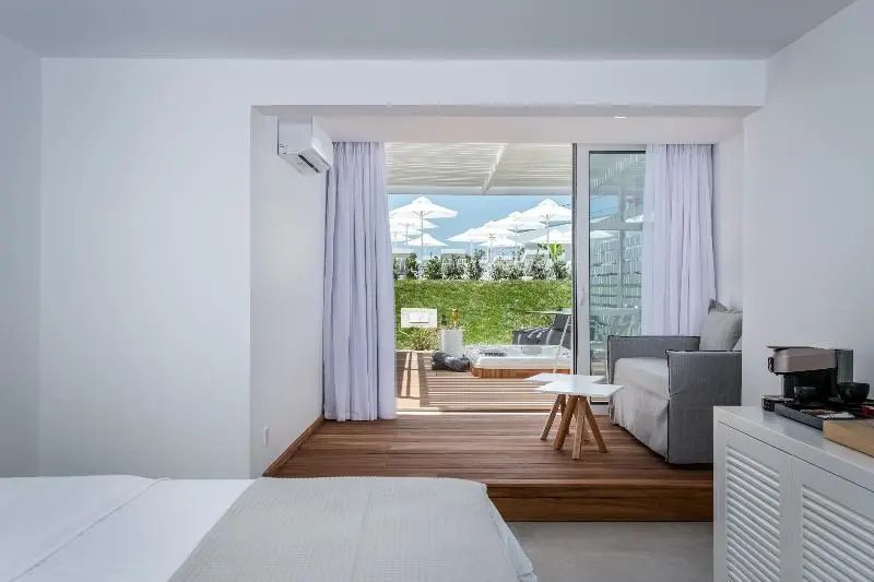 Helles Hotelzimmer mit Holzfußboden, Sitzbereich und Zugang zur sonnigen Terrasse.