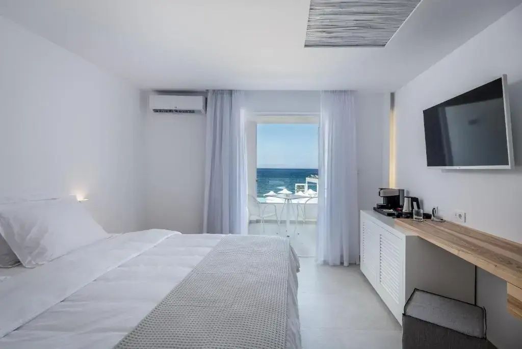 Weißes Hotelzimmer mit großem Bett und Zugang zum Balkon mit Meerblick.