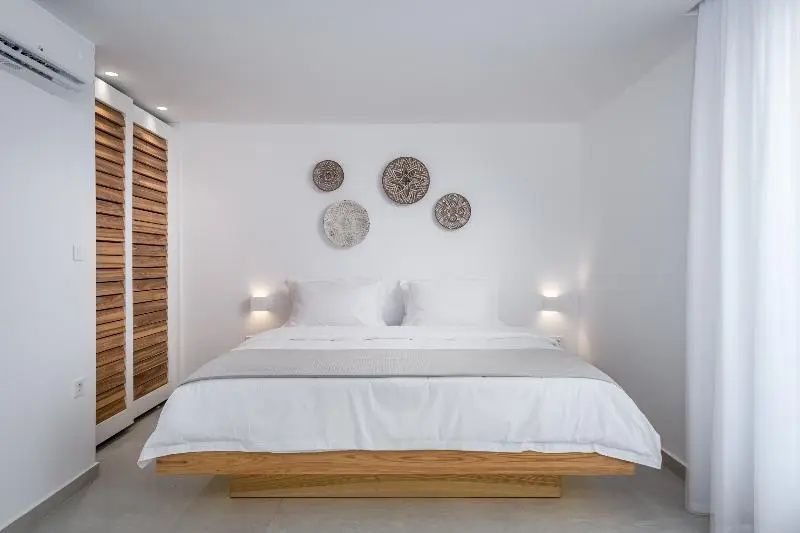 Doppelbett mit Holzrahmen, weißer Bettwäsche und runden Wanddekorationen aus Geflecht.