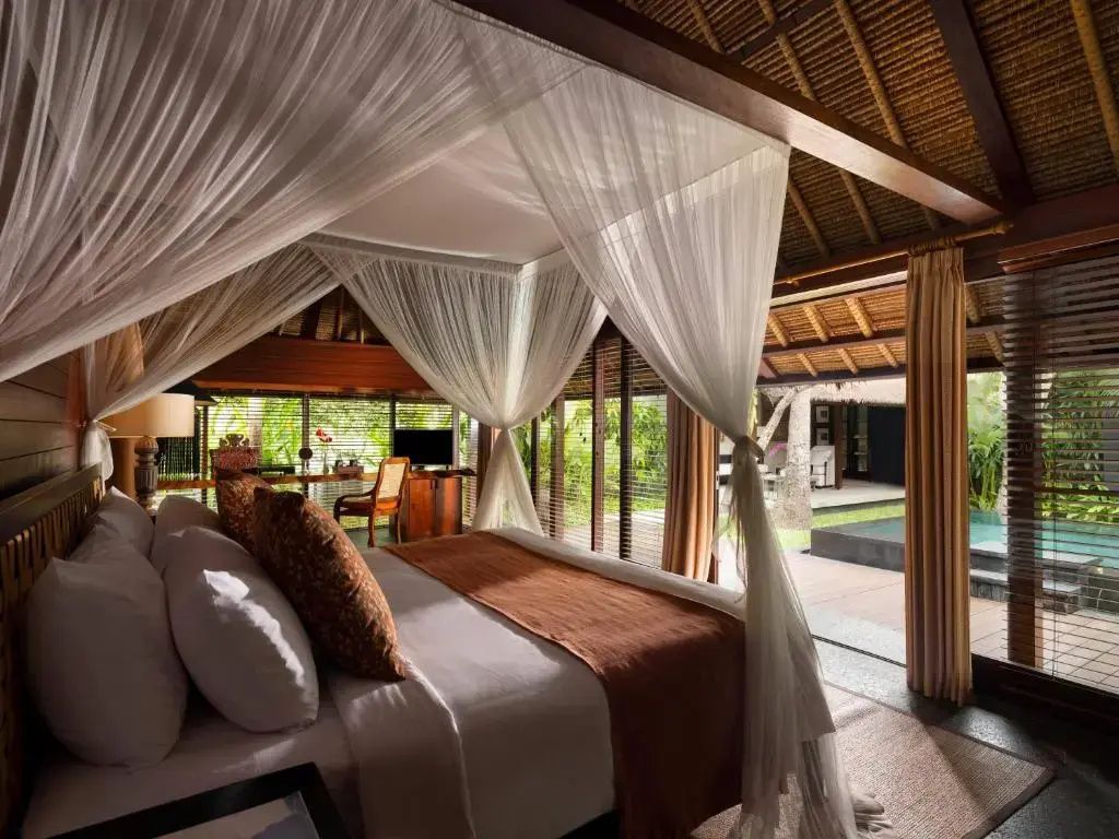 Himmelbett mit weißem Moskitonetz und Holzdecke in einer Villa mit Blick nach draußen.