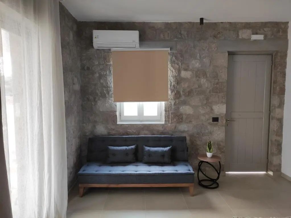 Dunkelgraues Schlafsofa vor einer rustikalen Steinwand unter einem kleinen Fenster