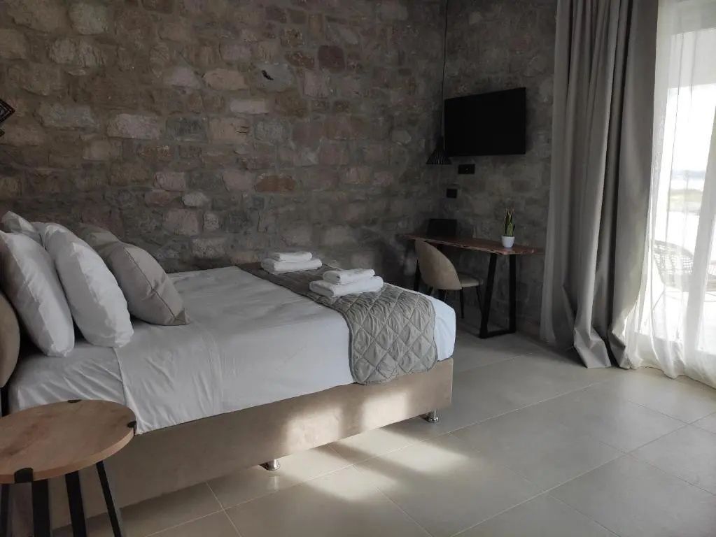 Schlafzimmer mit Doppelbett, Wandfernseher und kleinem Schreibtisch an einer Steinwand