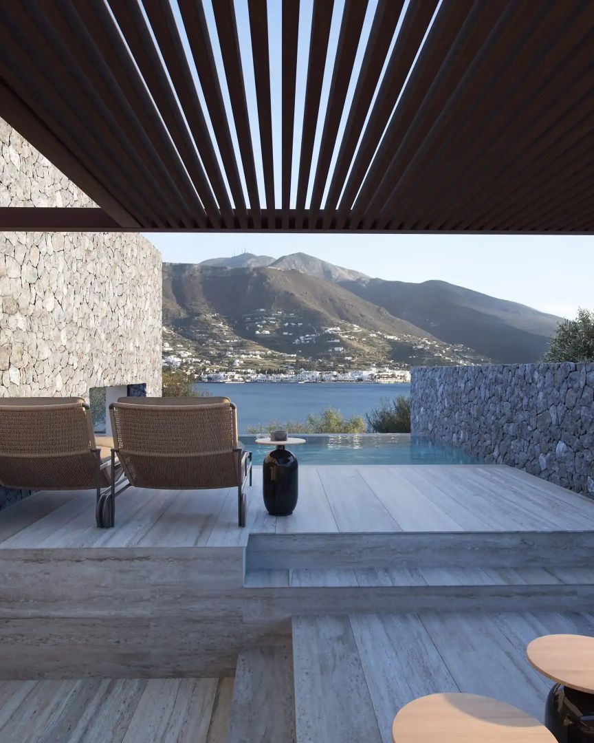 Überdachte Holzterrasse mit Liegestühlen und freiem Blick auf das Meer und Berge.