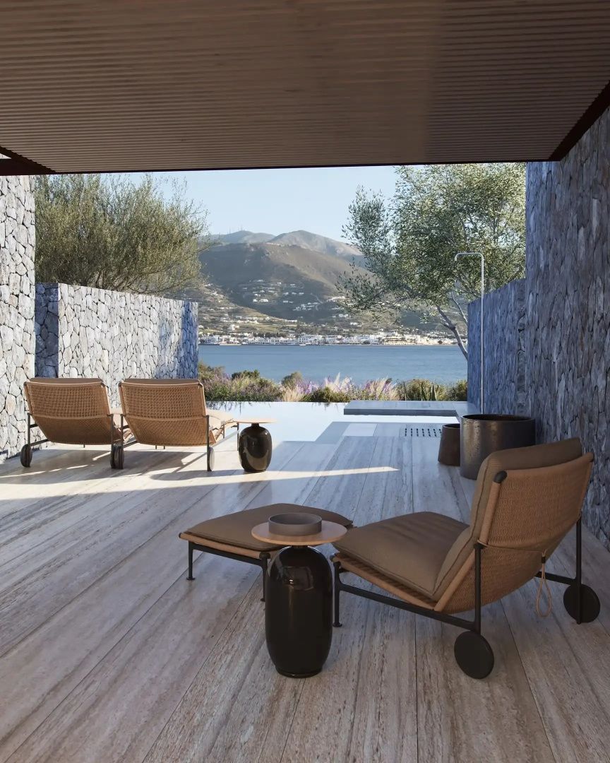Terrasse mit modernen Sesseln und Beistelltischen vor einer Meereskulisse.