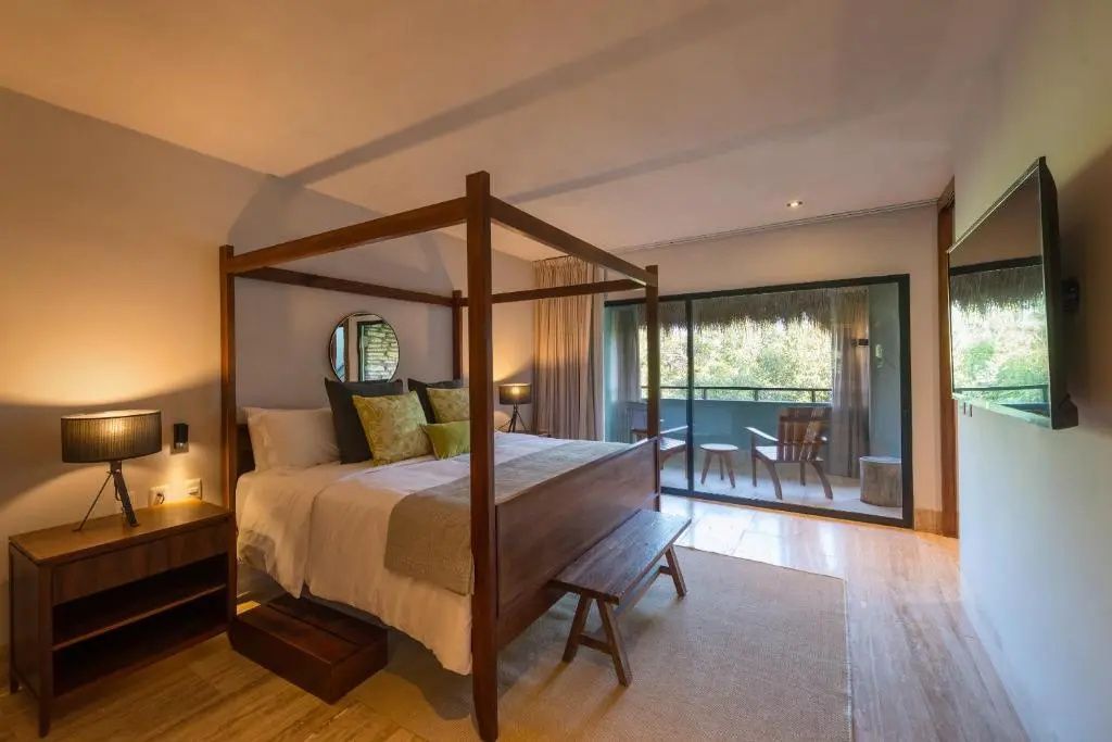 Schlafzimmer mit einem Himmelbett aus Holz, Kissen und Schiebetür zum Balkon.