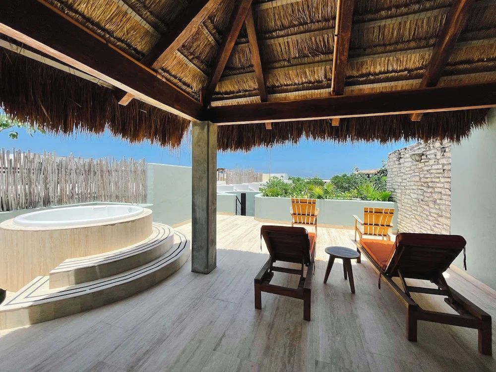 Überdachte Terrasse mit Strohdach, Liegestühlen und Whirlpool im Freien