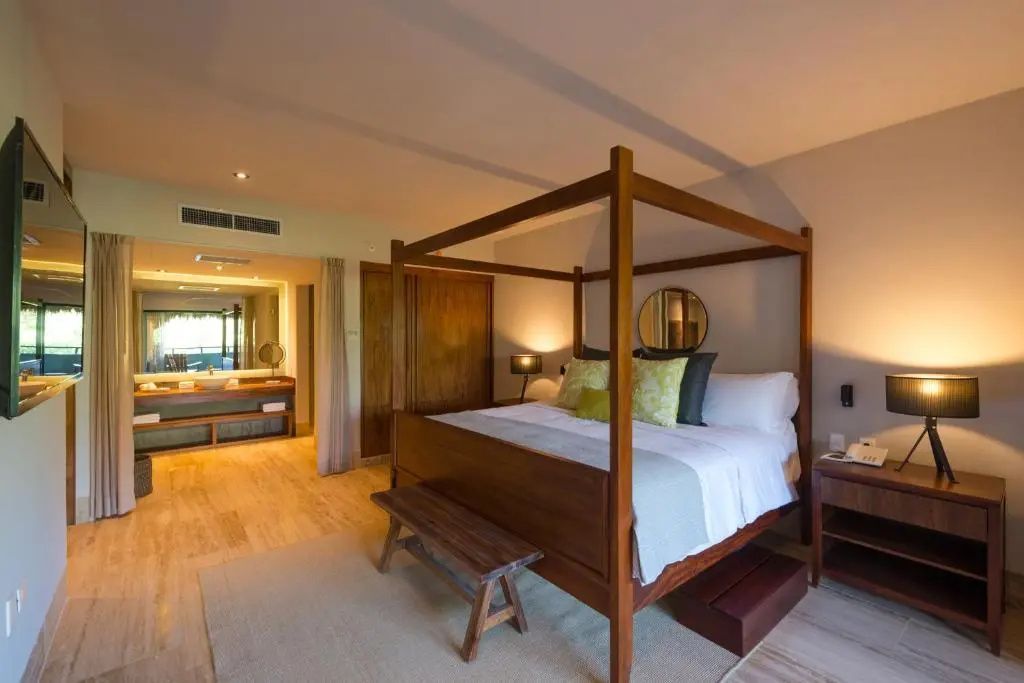 Geräumiges Hotelzimmer mit hölzernem Himmelbett, Sitzbank und Blick auf das angrenzende Bad.