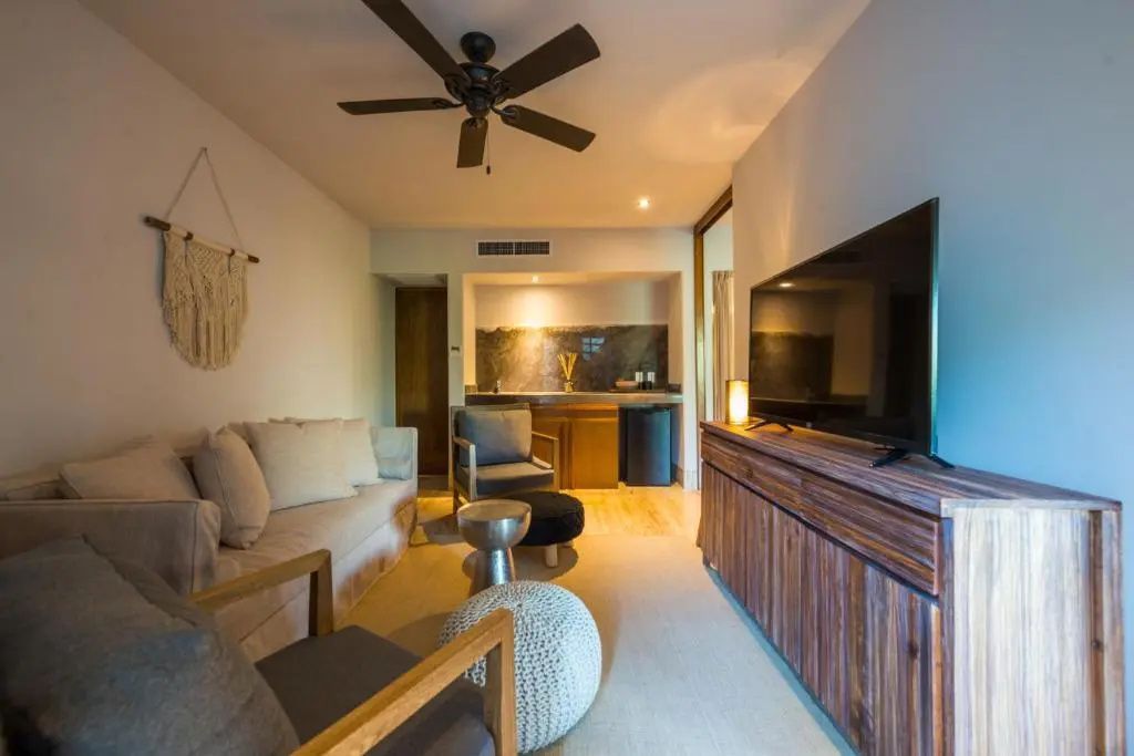 Wohnbereich einer Suite mit Sofa, Sessel, Fernseher auf Holzanrichte und Bar im Hintergrund.