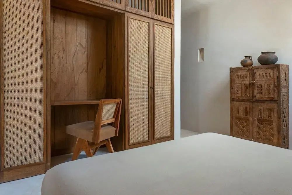 Schreibtisch aus Holz mit Holzstuhl neben einem Schrank mit Wiener Geflecht.