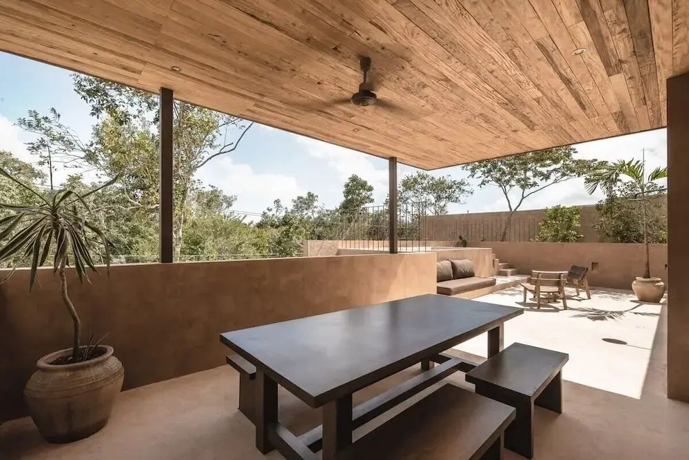 Überdachte Terrasse mit Holzdecke, Esstisch und Bänken sowie Blick ins Grüne.