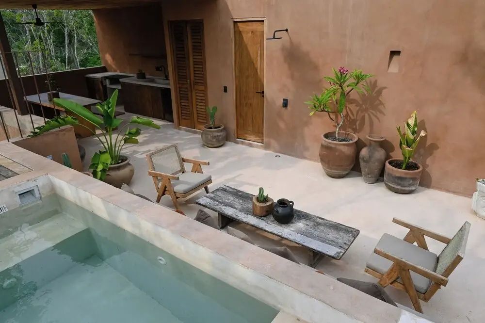 Innenhof mit kleinem Pool, Außendusche, Holzmöbeln und tropischen Pflanzen.