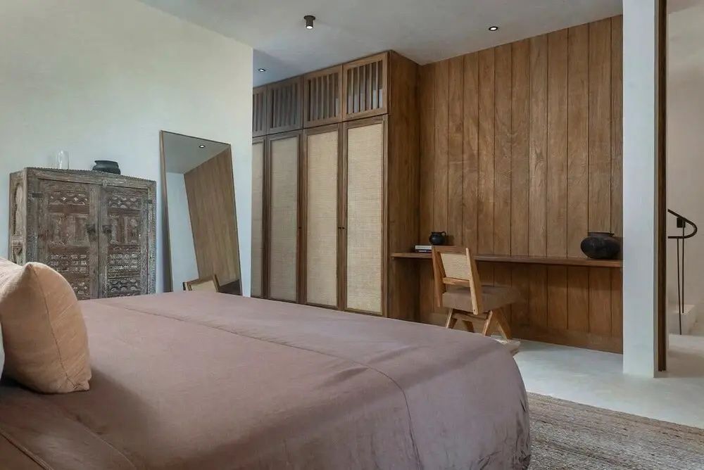 Schlafbereich mit großem Bett, Holzverkleidung an der Wand und bodentiefem Spiegel.