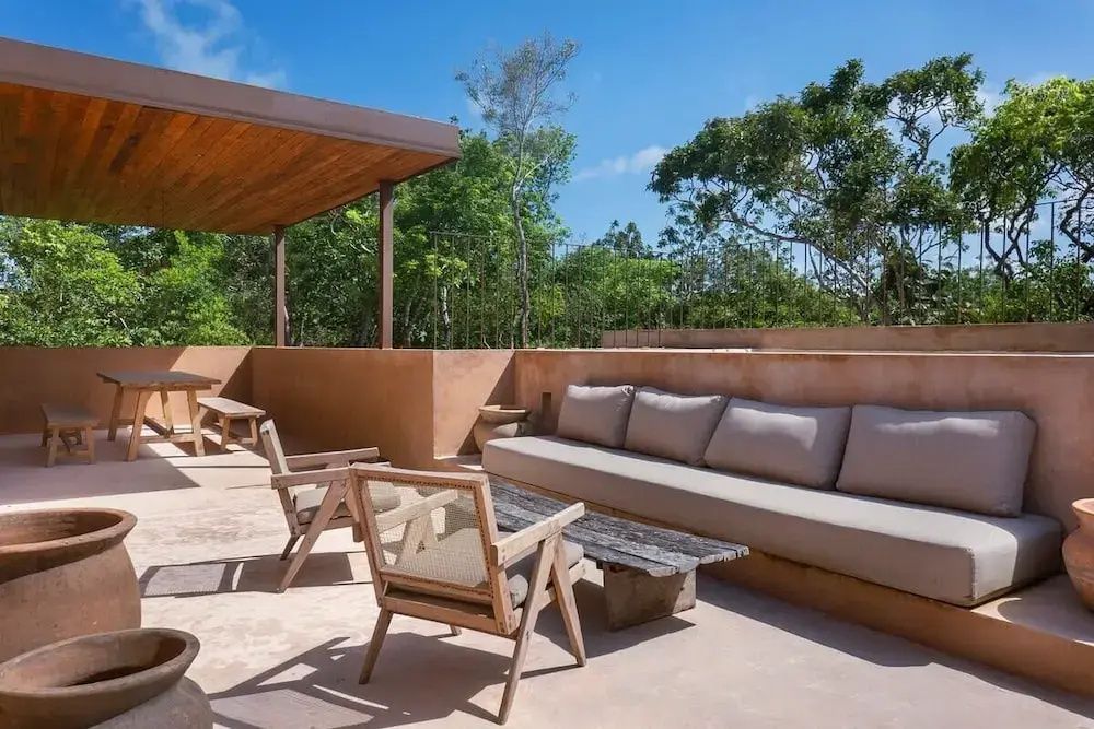 Sonnige Dachterrasse mit großer Sitzbank, Holzsesseln und Blick auf grüne Bäume.