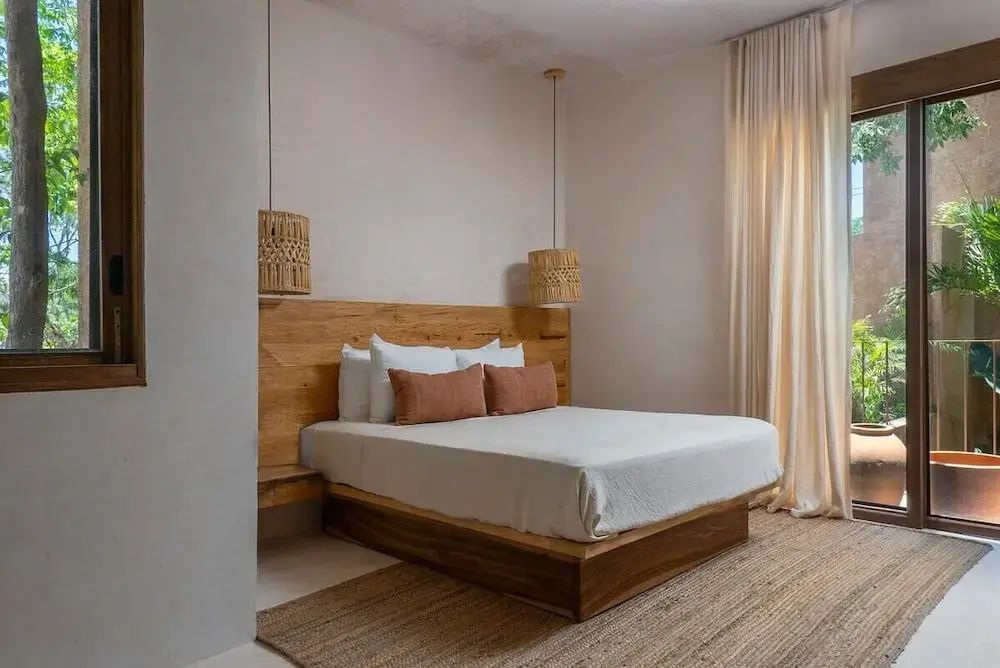 Doppelbett aus Holz mit geflochtenen Hängelampen und hellem Teppich im Schlafzimmer.