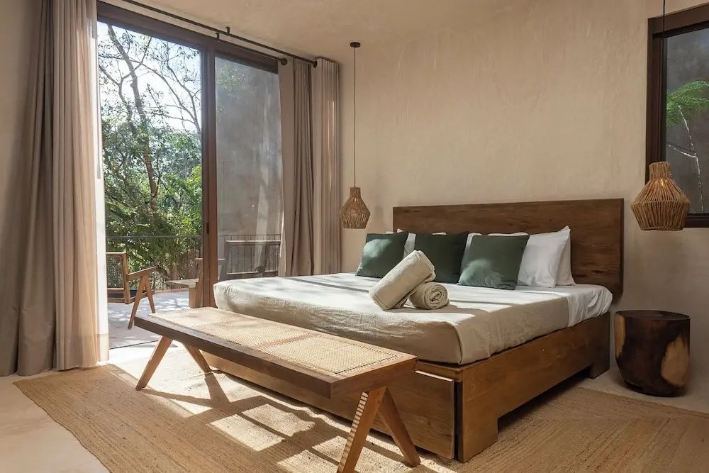 Schlafraum mit Doppelbett, Sitzbank und Blick durch eine große Glas-Schiebetür ins Grüne.
