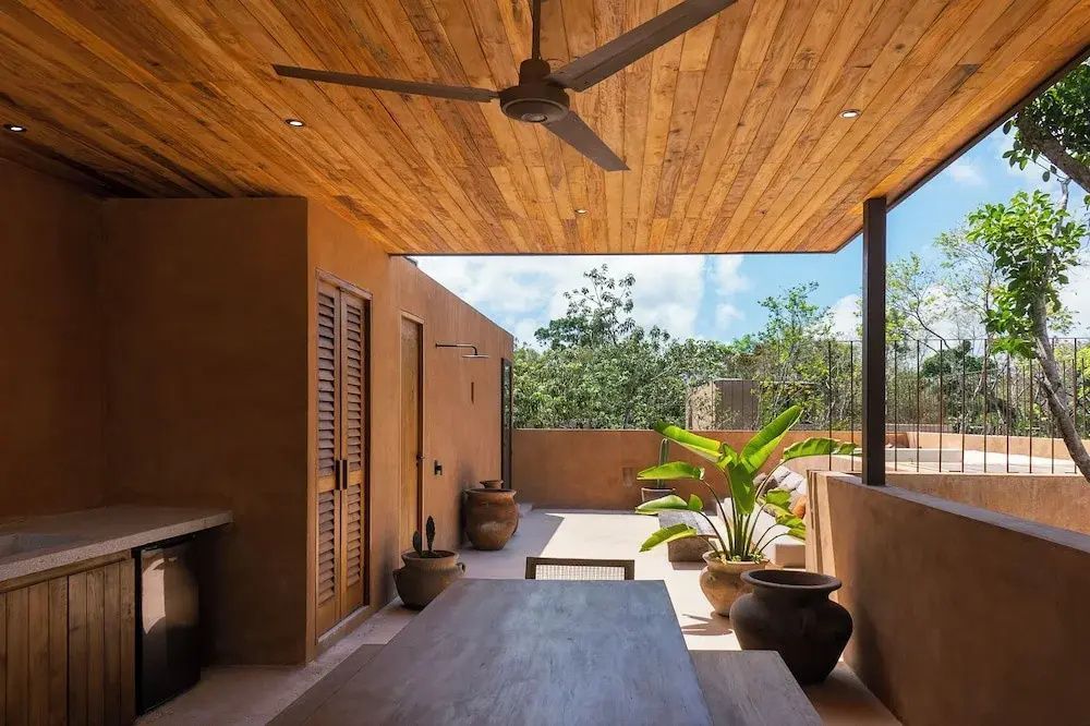 Überdachte Terrasse mit einem großen Esstisch aus Holz, Deckenventilator und Pflanzkübeln.
