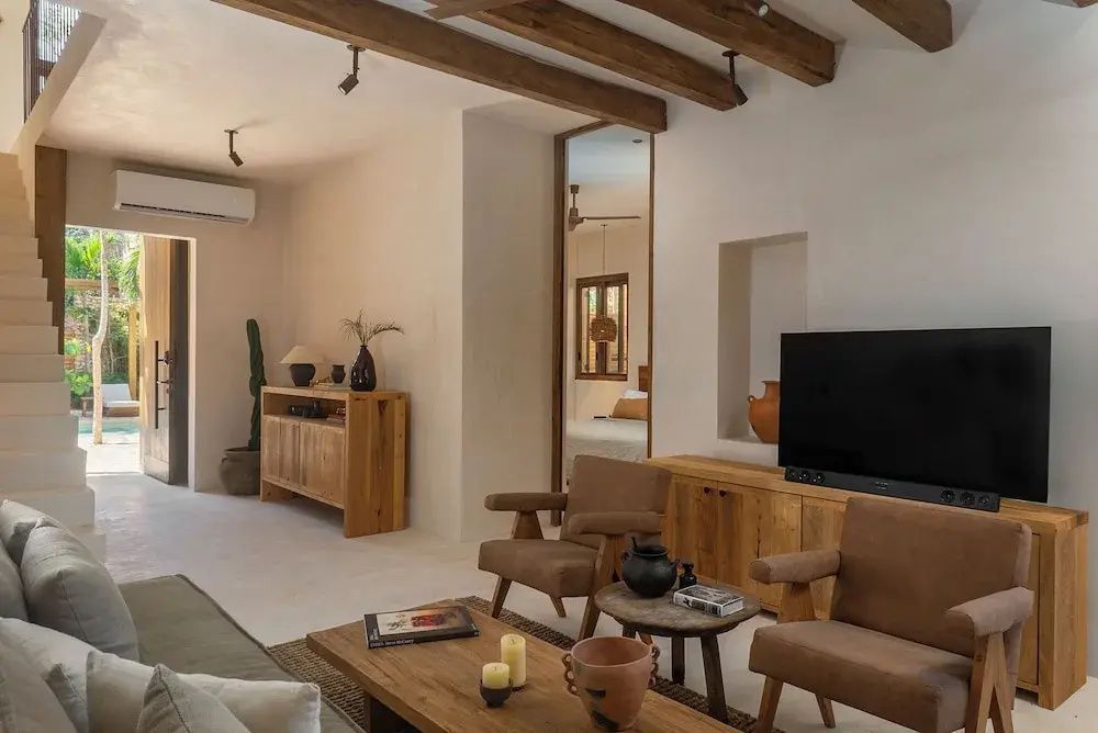 Wohnbereich mit Holzdecke, Fernseher, Sesseln und einem niedrigen Holztisch mit Dekoration.