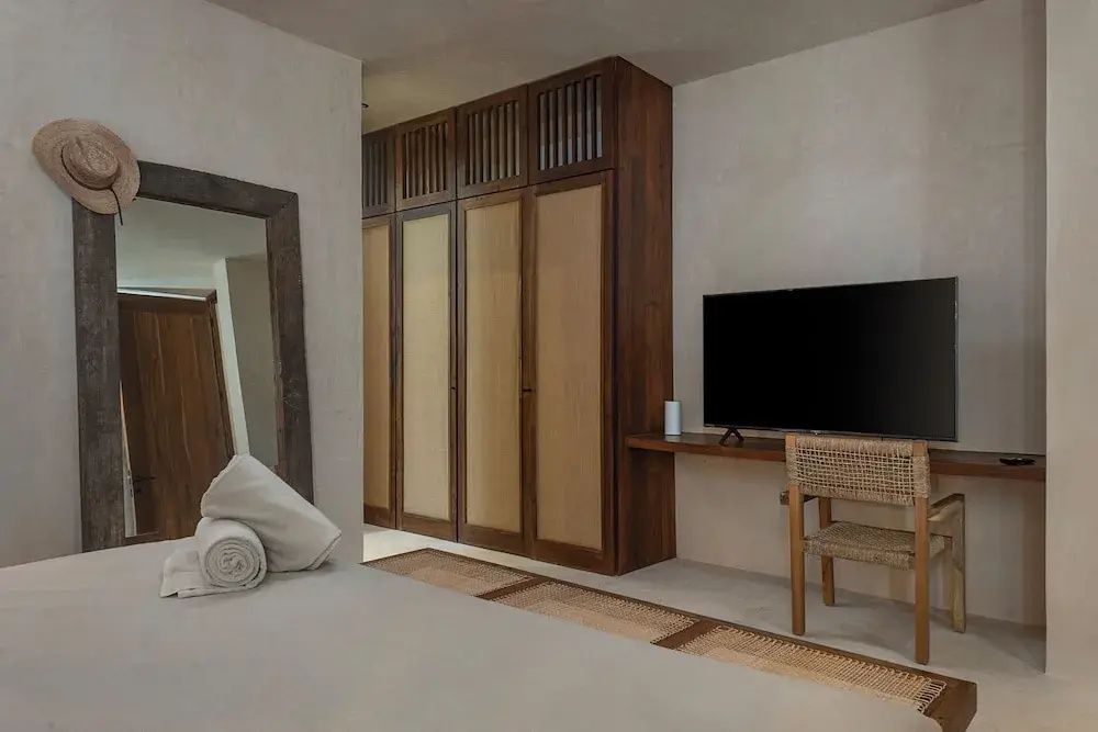 Zimmerbereich mit großem Holzschrank, Flachbildfernseher, Holzstuhl und Standspiegel.
