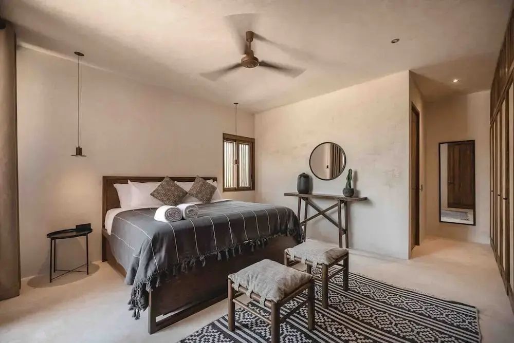 Schlafzimmer mit Doppelbett, Deckenventilator, Holzkonsole und gemustertem Teppich.