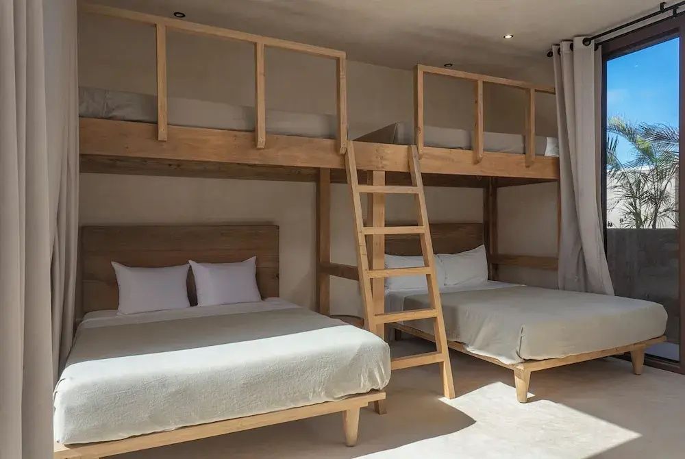 Hotelzimmer mit zweistöckigen Holzbetten und hellen Textilien.
