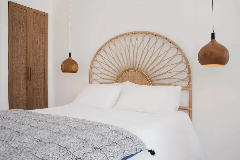 Doppelbett mit weißer Bettwäsche und auffälligem Rattan-Kopfteil im hellen Schlafbereich.