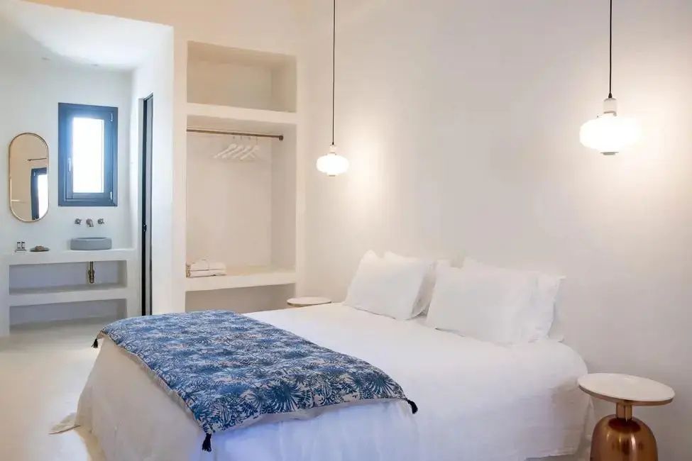 Weiß gestaltetes Hotelzimmer mit Doppelbett, blauer Tagesdecke und offenem Wandregal.