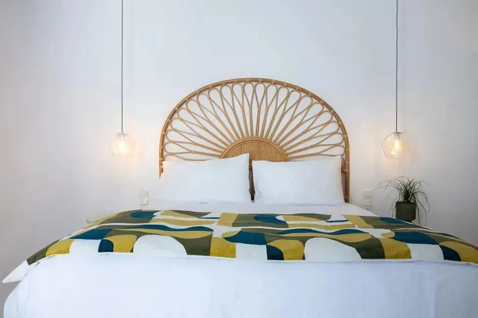 Doppelbett mit weißer Bettwäsche, gemusterter Tagesdecke und Kopfteil aus Rattan.