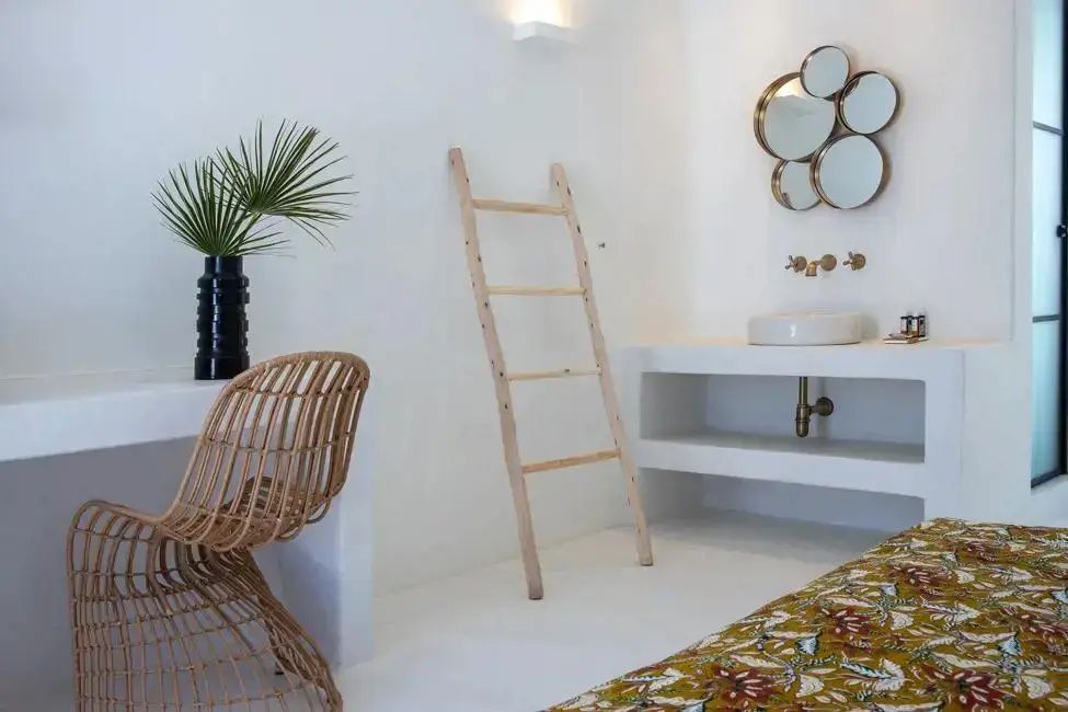 Heller Raum mit einem Waschtisch, Rattanstuhl, Holzleiter und runden Spiegeln an der Wand.